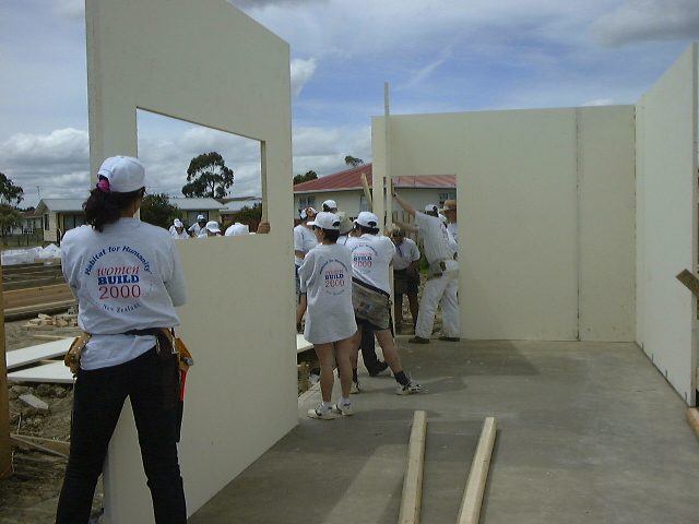 females in the trades build a house carry a constructed wall. 